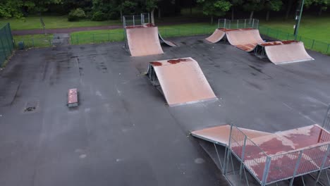 aerial view flying above fenced skate scooter park ramp in empty closed playground