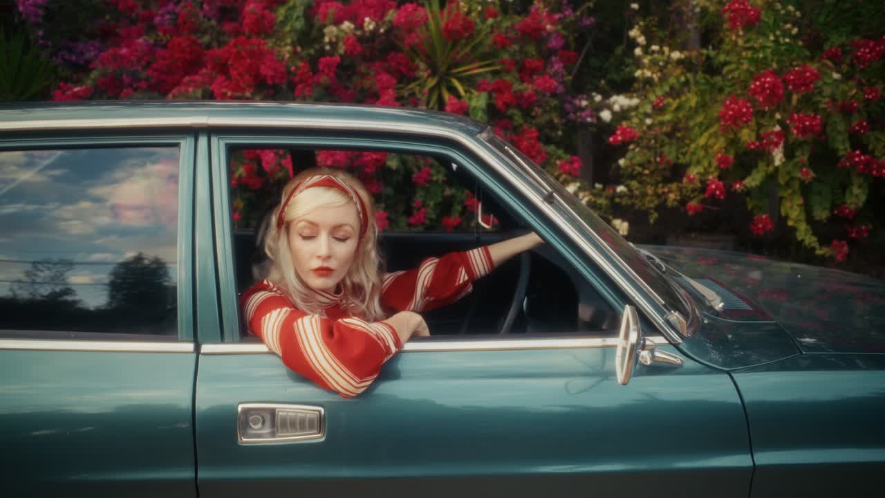 Stylische blonde Frau in einem Oldtimer neben blühenden Blumen