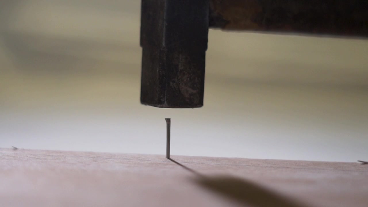 Un martello che conficca un chiodo su una tavola di legno. - Primo piano rallentato.