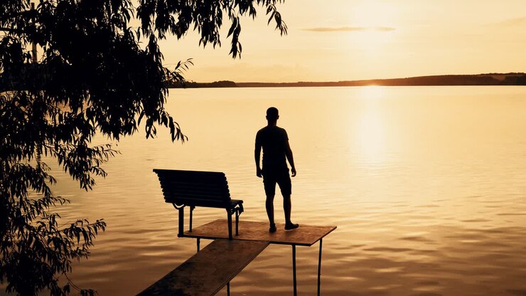 A young man goes to the bridge on the river and looks on a beautiful view of the sunset. Orange background.