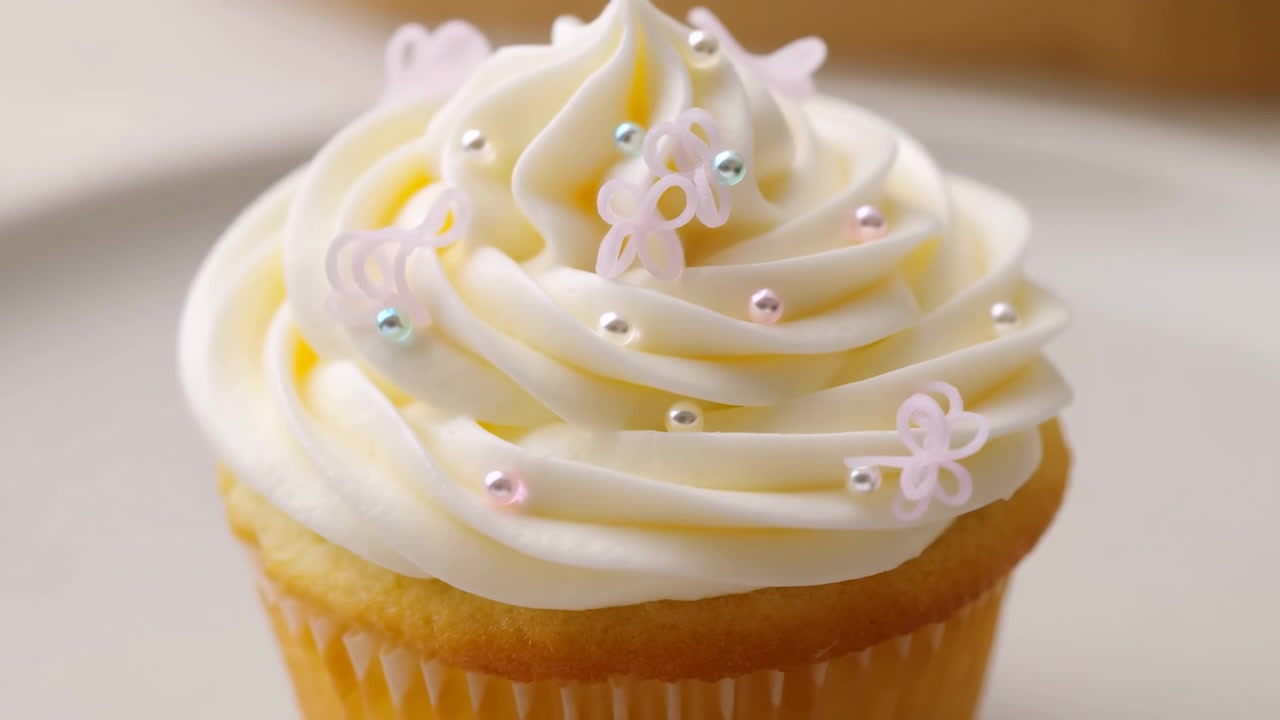 Cupcake cremoso alla vaniglia con decorazioni di perle, morbido vortice di crema al burro e piccole perline di zucchero pastello, in studio.