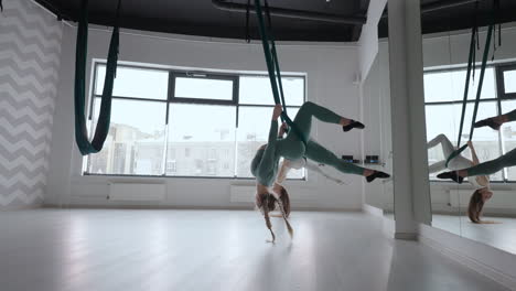 dos jóvenes mujeres yogi practicando yoga aéreo en hamacas verdes en un club de fitness. hermosas mujeres trabajando en clase realizando aero yoga. variación de la postura de la pirámide parsvottanasana