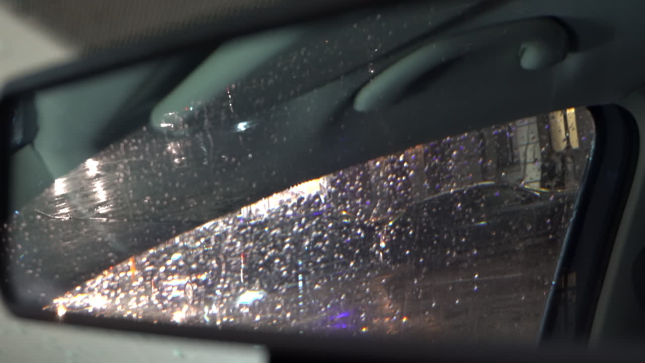 Rain dripping down the window of a moving car in the evening reflected in the rearview mirror