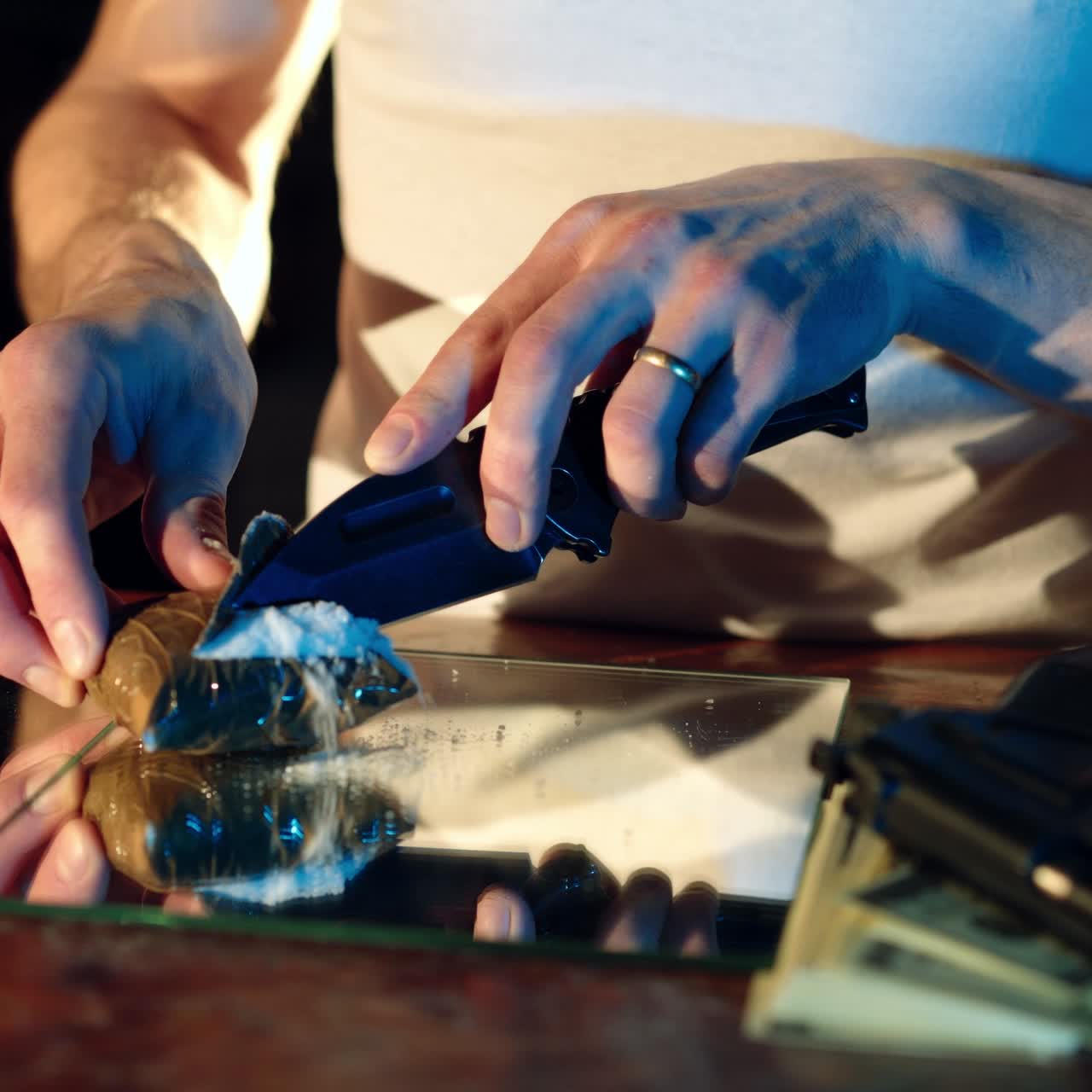 a thug is cutting a package with drugs on the table by knife. Drug trafficking