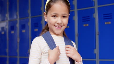 smiling girl holding backpack in school hallway with blue lockers