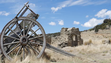 Sliding-shot-of-a-small-and-old-wooden-cart,-surrounded-by-dry-grass,-with-ruins-in-the-background,-on-a-sunny-day