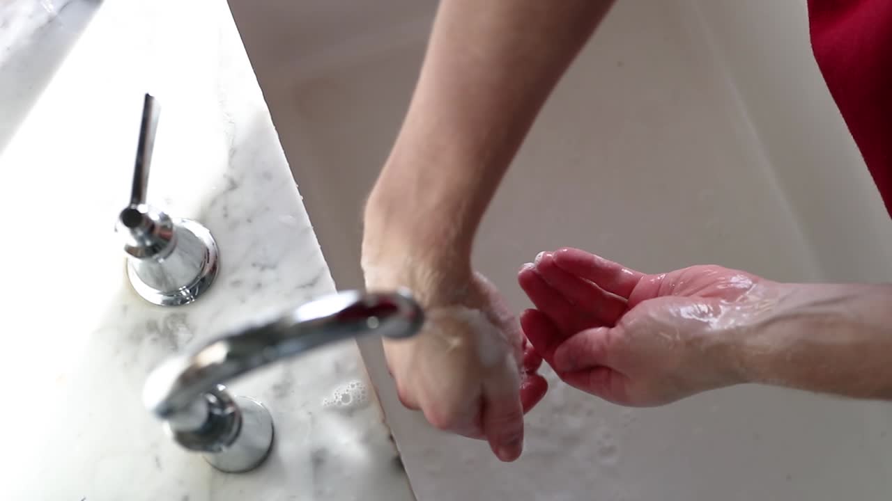 Mand vasker sæbe af hænder i slow motion, set ovenfra.