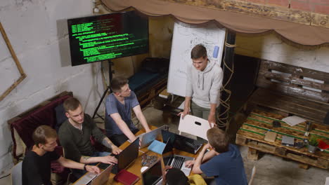 high angle view of multiethnic group of young people sitting at desk and using laptop computers, one standing in front and discussing project with them