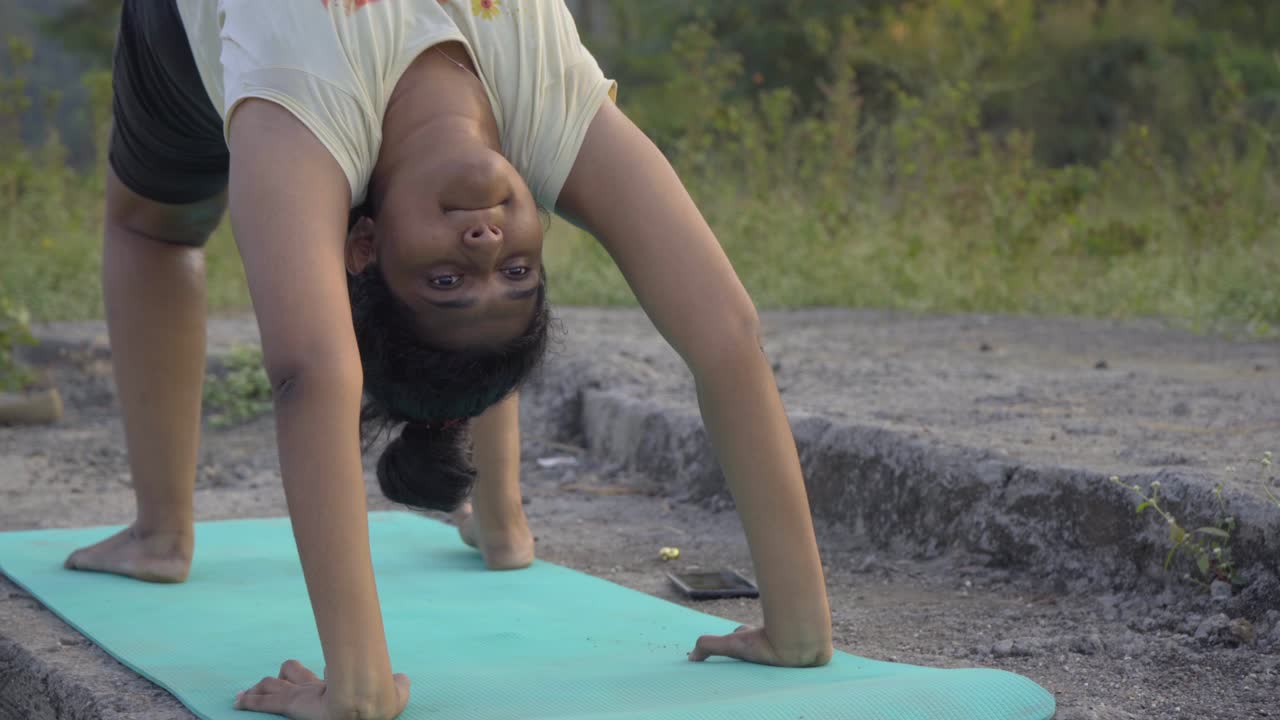 Indian girl doing upward bow weel pose urdhva dhanurasana yoga pose by the lakeside face close front shot