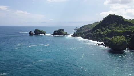drone shot of coral island on the beach,hit by waves during sunny day - timang island, yogyakarta, indonesia