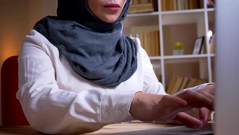 closeup shoot by camera moving from hands typing on the laptop to adult muslim female employee in hijab on the workplace indoors