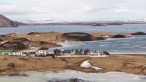 scenic view of the frozen lake mývatn and surrounding volcanic pseudocraters in skútustaðir, iceland, with a small village in the foreground.
