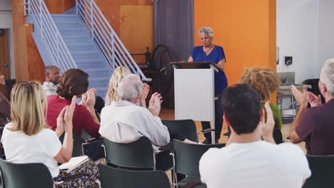 group attending neighborhood meeting applauding speaker on podium in community center