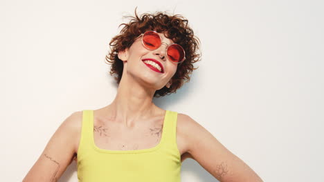 woman with short curly hair in yellow tank top and red sunglasses