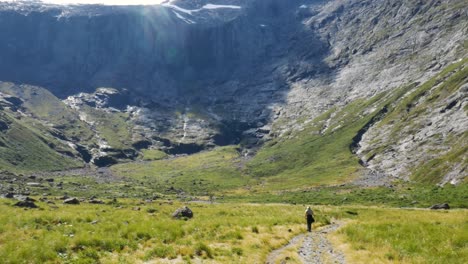 toma aérea de arriba hacia abajo de un excursionista caminando cuesta abajo impresionante paisaje montañoso en verano - parque nacional de fiordland, nueva zelanda