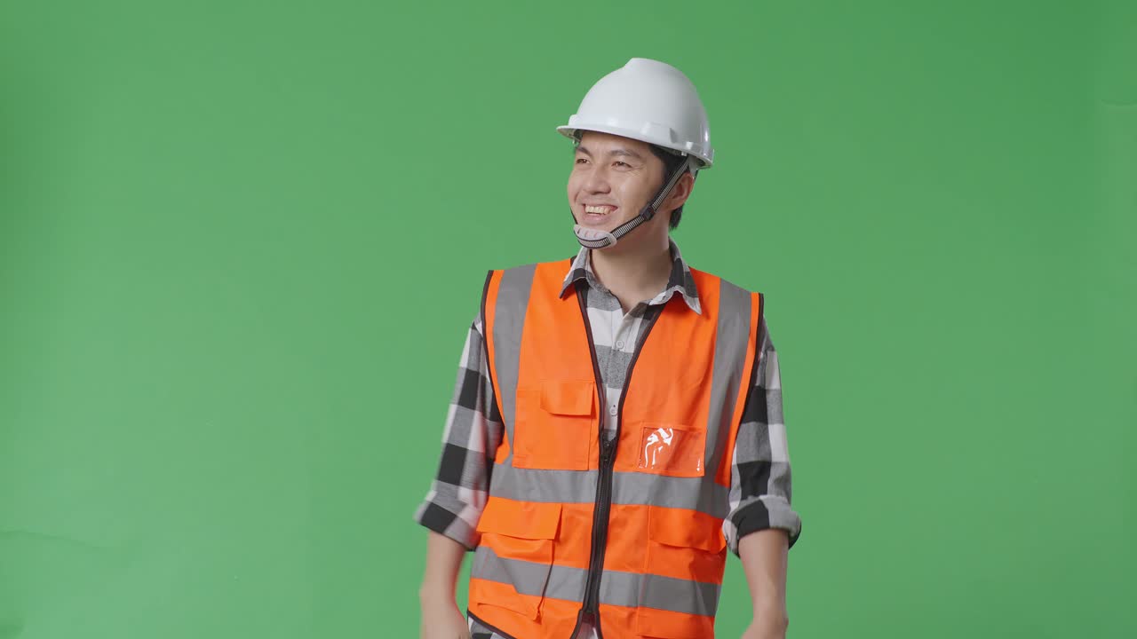 안전 헬을 입은 아시아 남성 엔지니어가 녹색 스크린 배경 스튜디오에서 는 동안 손을 흔들고 있습니다.