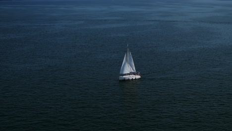 aerial view of sailboat is sailing on calm water with its sails full, illuminated by the warm light of the setting sun