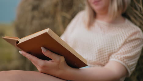 close-up de mulher segurando um livro aberto, dedos suavemente virando a página, enquanto ela lê com foco, fundo suave e desfocado melhora o ambiente de campo pacífico