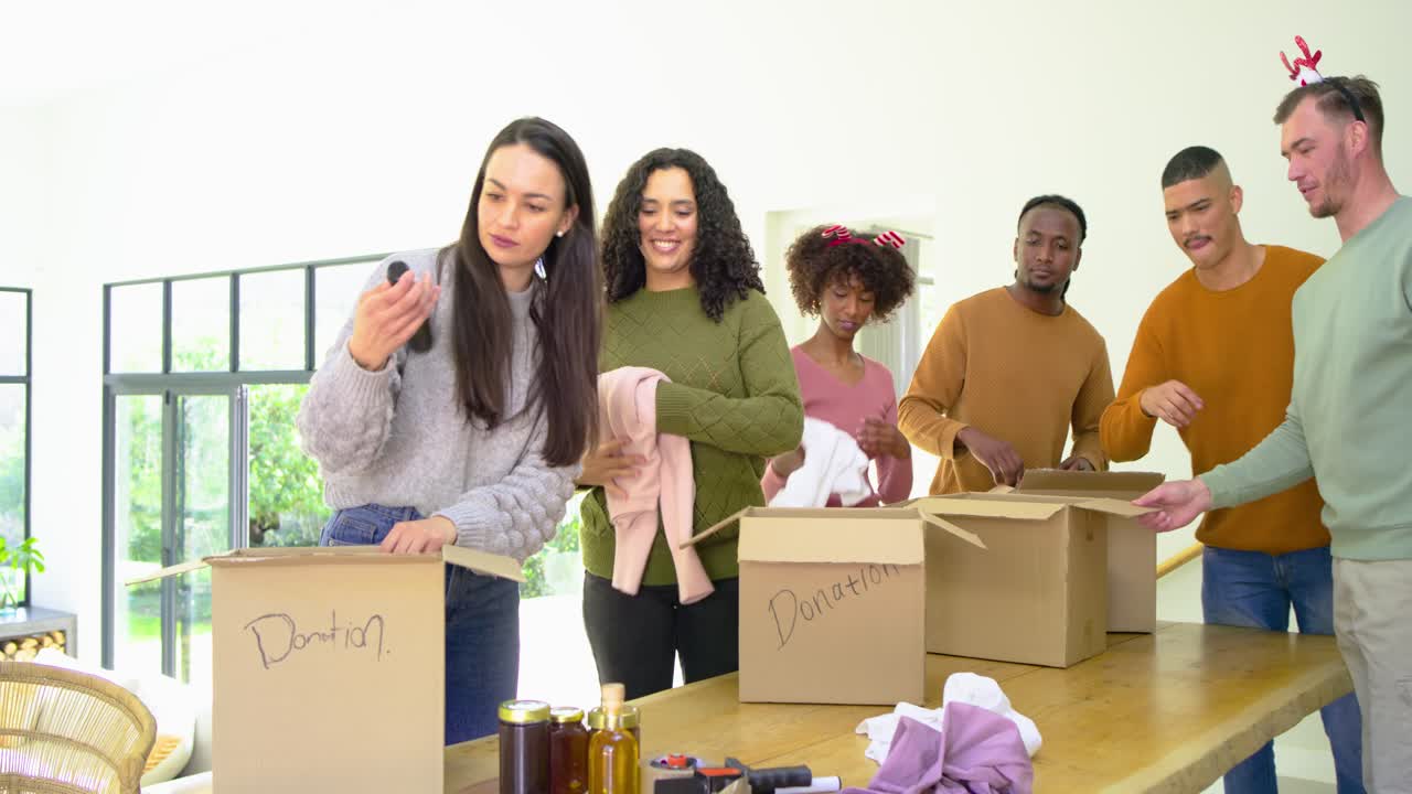 Diverse volunteers opening donation boxes at wooden table sorting clothing and jars for pickup