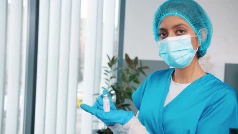 Close-Up-Of-Young-Hindu-Female-Healthcare-Specialist-Virologist-In-Protective-Uniform-And-Medical-Mask-Holding-In-Hands-In-Gloves-Ampoule-With-Coronavirus-Vaccine,-Covid-19-Vaccination,-Virus-Cure