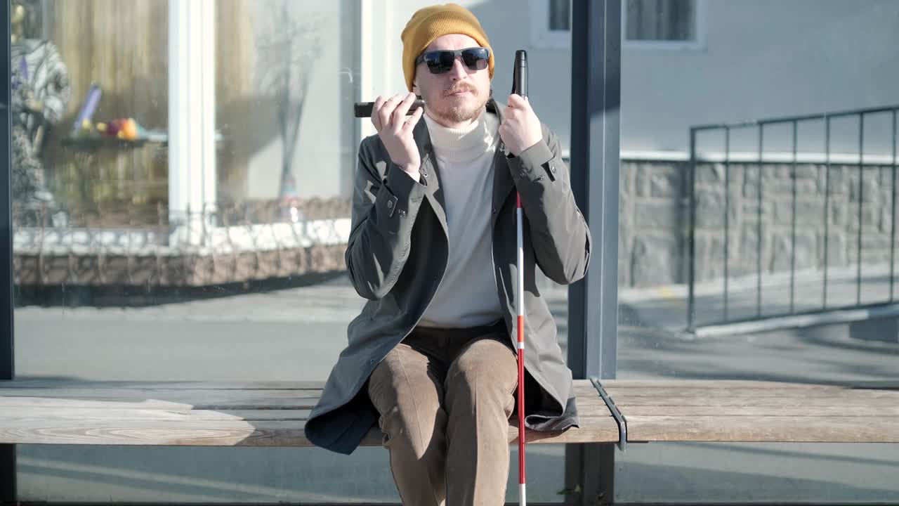 Visually impaired man talking on the phone, sitting on the bench in the city.