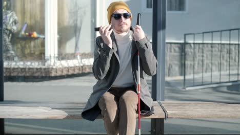 un hombre con discapacidad visual hablando por teléfono, sentado en un banco en la ciudad.