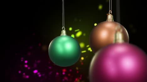 swinging colourful christmas baubles over colourful dancing lights on black background