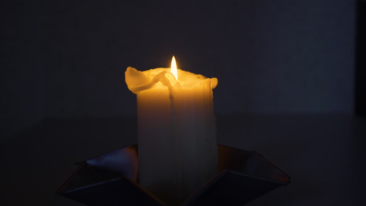 Slow moving medium shot around a lit candle in a dark room