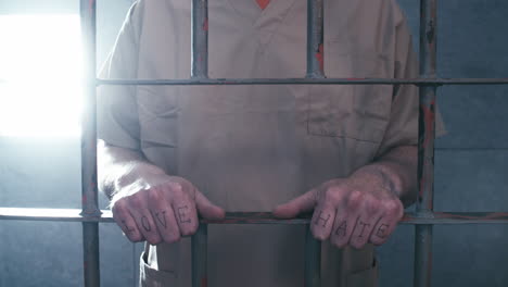 medium shot of a prisoner with "love" and "hate" tattooed across his knuckles as the camera dollies in, then he walks away