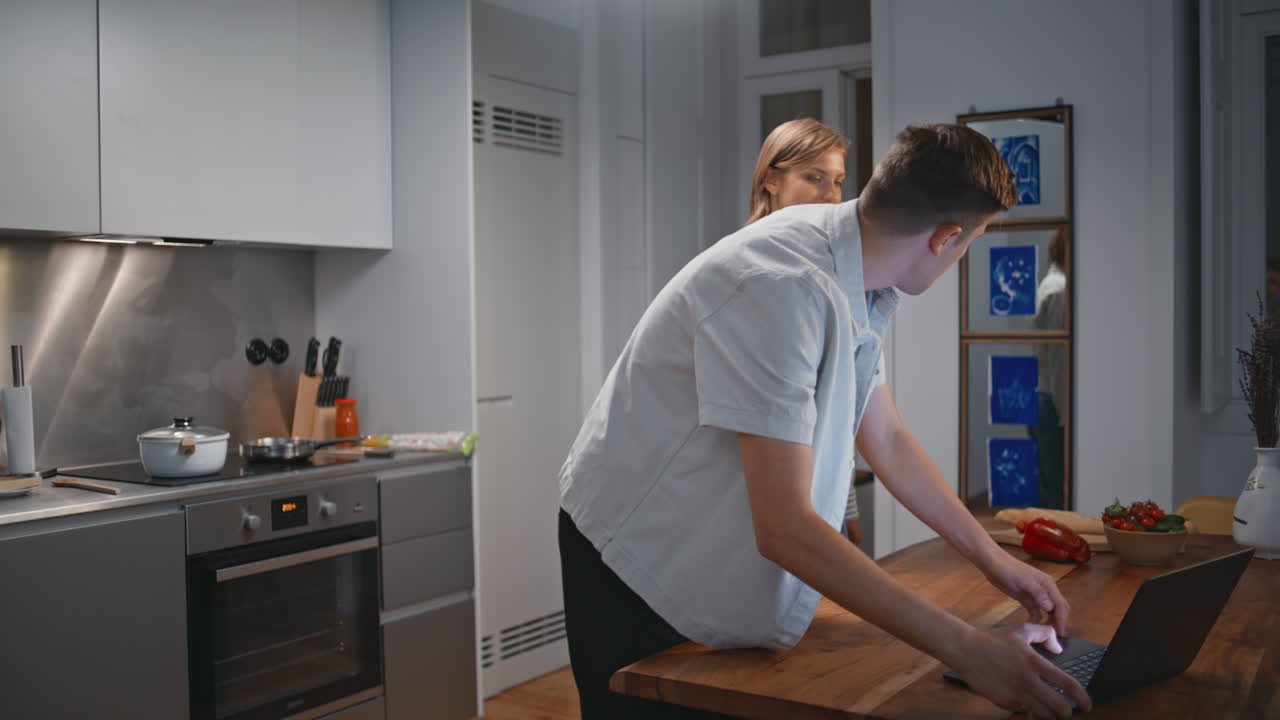 Unge ektefeller som lager mat sammen hjemme. Glade mennesker som ser på kulinarisk video