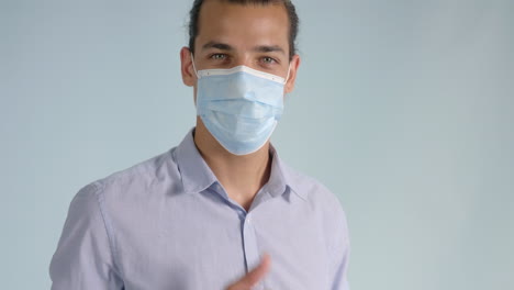 smiling young man puts on face mask and raises thumbs up turning to camera