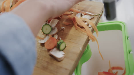 Hands-of-biracial-woman-composting-vegetable-waste-in-kitchen,-slow-motion