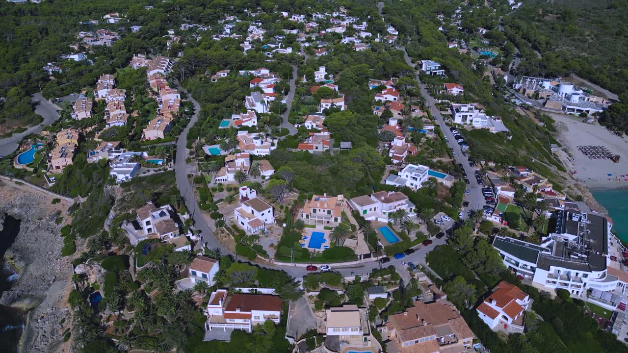 Stunning drone view of a luxury residential real estate area on the coast of Mallorca, Spain. The scene shows villas, resort hotels, and homes built on the cliffside overlooking the Mediterranean Sea