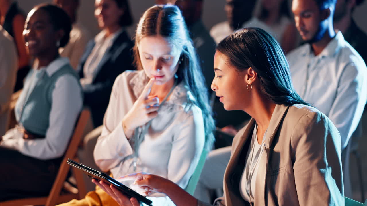 Two Businesswomen Discussing Content on a Tablet at a Conference