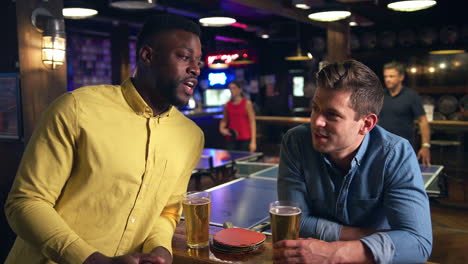 amigos masculinos se reúnen para tomar bebidas en un bar con clientes jugando al tenis de mesa detrás