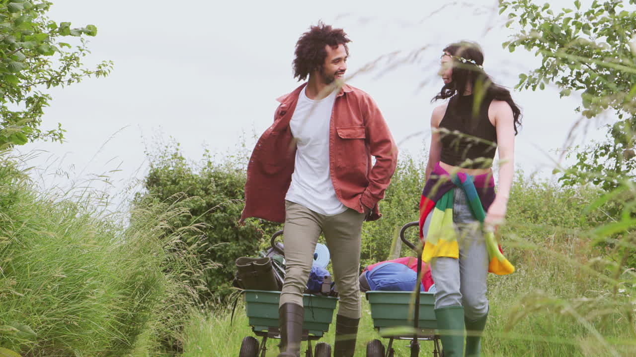 una pareja joven tirando de un carrito lleno de equipos de campamento a través del campo hacia el festival de música.