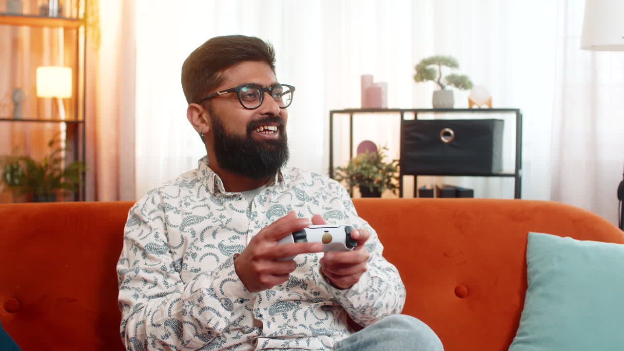 Indian man playing video game with joystick controller while at home focused and excited mood
