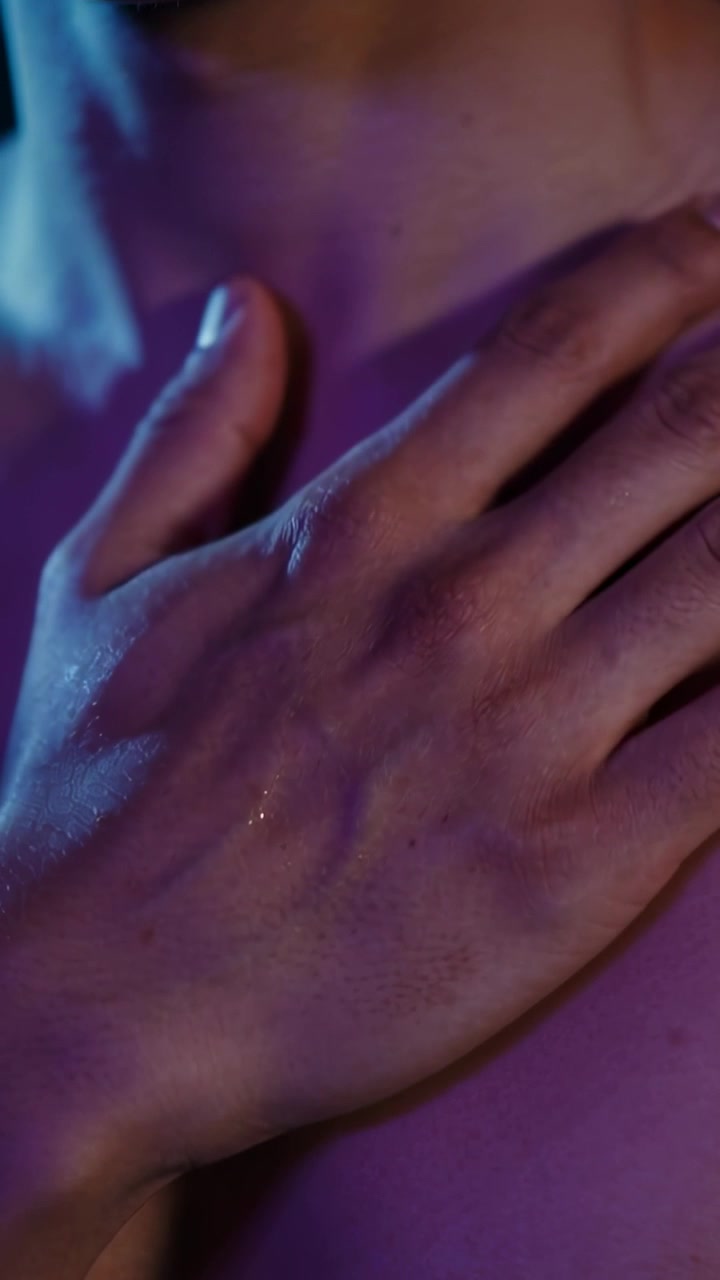 Vertical video: Placing adult hand on bare upper chest under blue-purple light, showing sweat