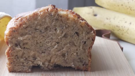 left pan of banana bread cut in half on a wooden board with a banana in the back.