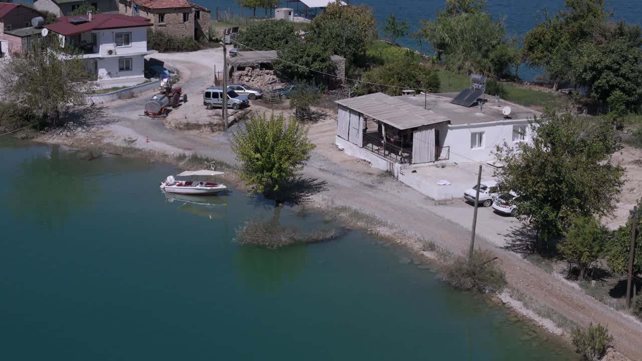 Aerial view following farmer driving old tractor through rural Green lake rustic village in the Taurus mountains of Turkey