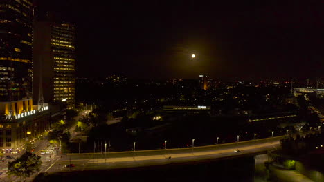 luna llena colocada sobre tachuelas de trenes urbanos con el cruce arterial del puente en primer plano
