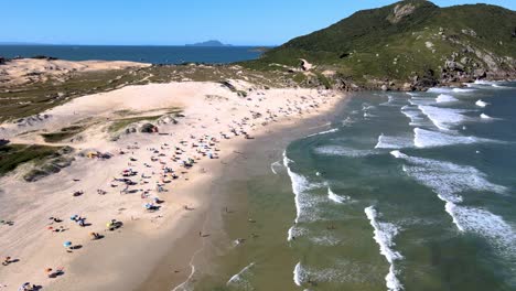 scena aerea di drone di spiaggia paradisiaca urbanizzata con persone che camminano sulla sabbia con dune montagne e spiaggia di mare di santinho florianã3polis nel tardo pomeriggio