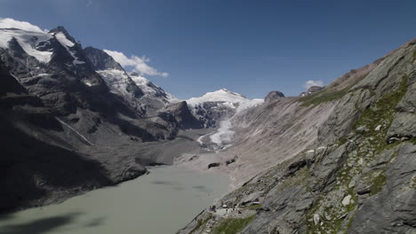 Disparo-De-Drone-Que-Revela-El-Lago-Glaciar-Pasterze-Derritiéndose-Al-Pie-De-La-Montaña-Grossglockner-En-Los-Alpes-Austriacos,-Turista-En-El-Parque-Nacional-De-Alto-Tauern-En-Austria