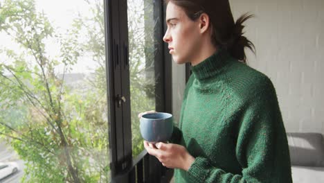 Caucasian-non-binary-transgender-woman-looking-through-window-and-thinking