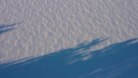 aerial topdown flying sideways over shadows and patterns in the fresh snow