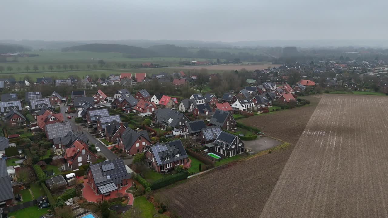 Suburb one family houses with swimming pool and solar panels on roof during cloudy day. German neighborhood in winter season. Aerial birds eye flyover shot. Production of green energy with units.