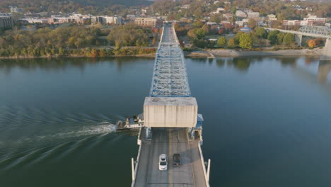 aerial footage following a tug boat that is sailing under a bridge in downtown chattanooga on the tennessee river during sunset