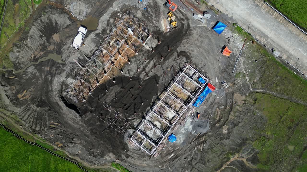 Construction site seen from above showing project layout and nearby roads, ascend orbit over exposed beams and dirt stock piles