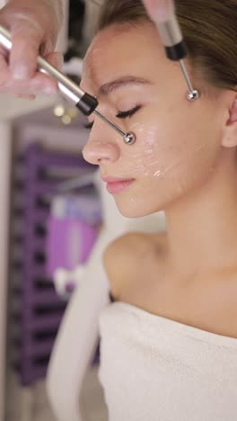 woman at spa getting facial treatment relaxing with eyes closed a woman with black hair is receiving a relaxing facial treatment at a spa as the esthetician massages her jaw she closes her eyes in blissful gesture