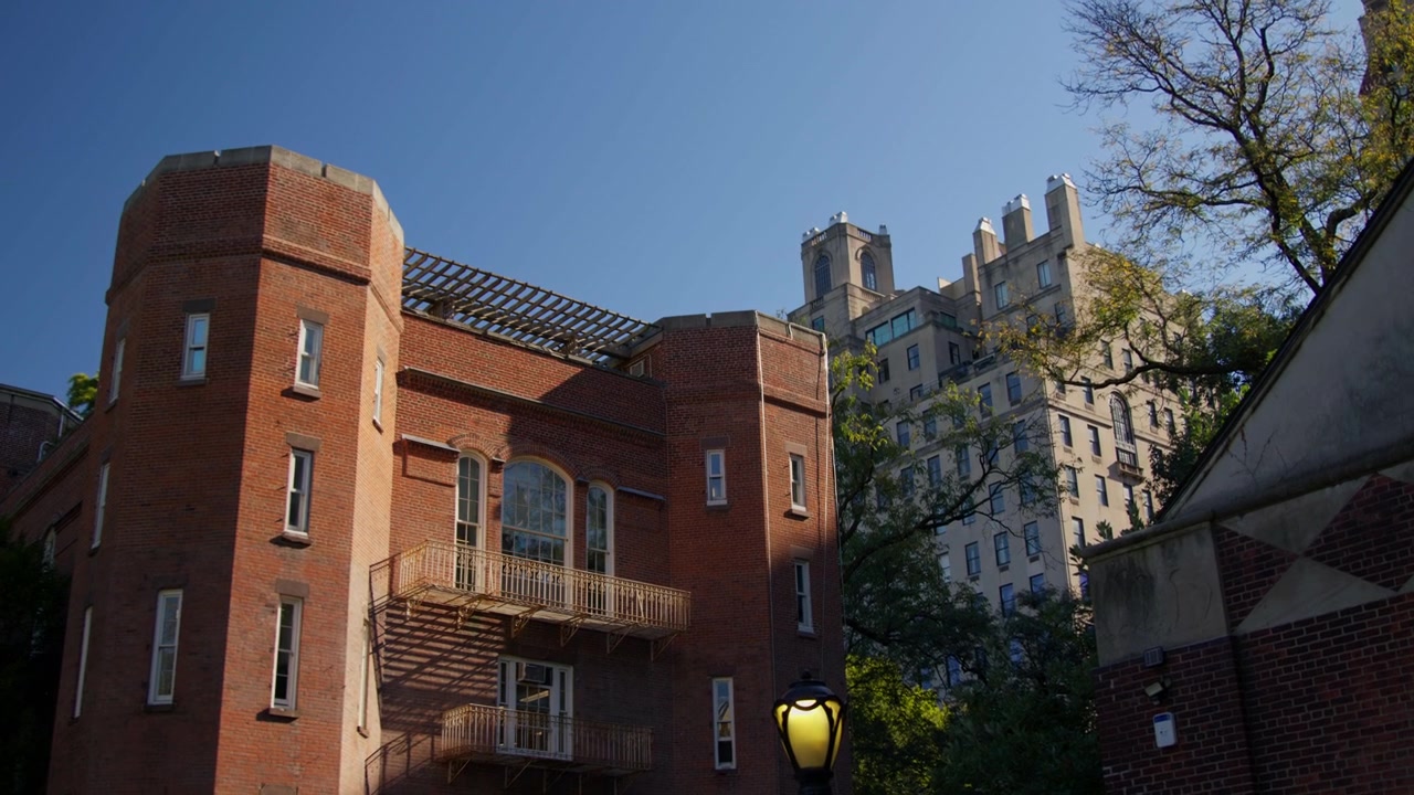 Edificio in mattoni rossi con balconi in ferro battuto e un lampione a globo sotto il forte sole pomeridiano, con le torri gemelle ornate di un iconico condominio che si ergono dietro.